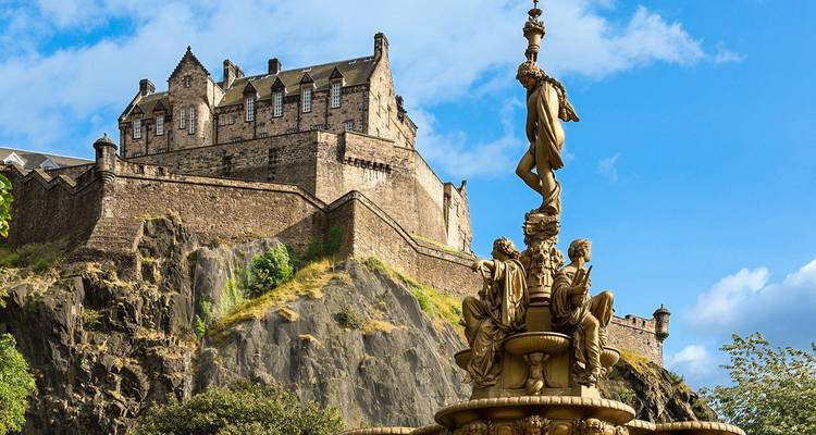 Gros plan d'un château historique avec des statues au premier plan sous un ciel bleu.