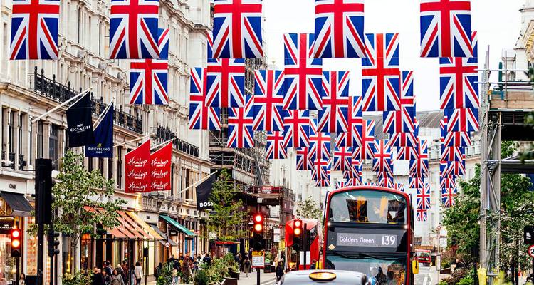 Belebte Oxford Street Szene mit mehreren Union Jack Flaggen, Geschäften und einem ikonischen Doppeldeckerbus.