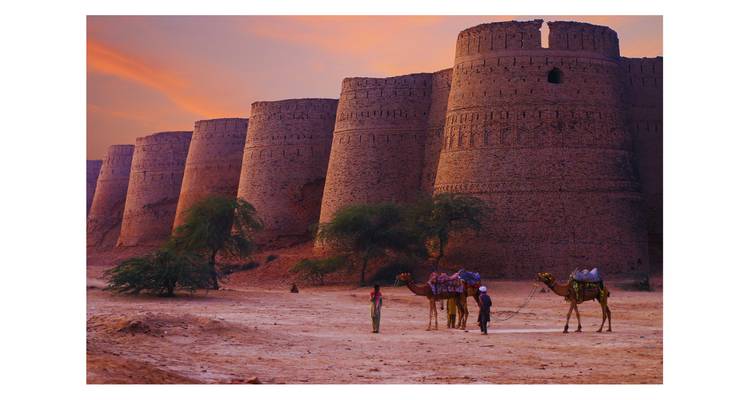 Camel riders beside massive sandy-coloured bastions of Derawar Fort at sunset under orange sky.