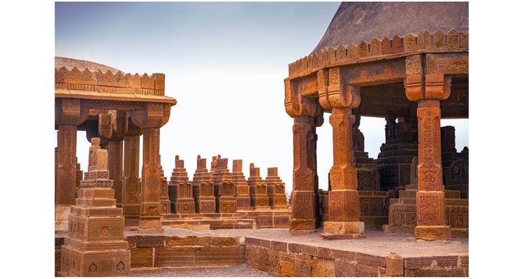 Ornately carved sandstone tombs and pillars at the ancient Makli necropolis under pale sky.