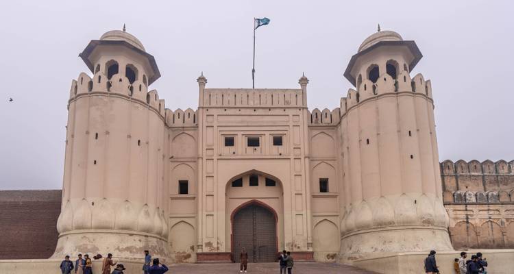 Foggy morning view of Lahore Fort’s imposing Alamgiri Gate with visitors entering beneath national flag.