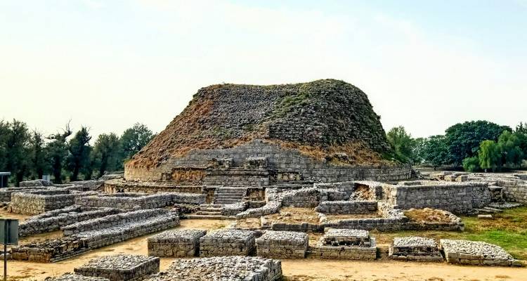 Des fondations en pierre entourent le dôme altéré d'un ancien stupa bouddhiste se détachant contre un ciel pâle.