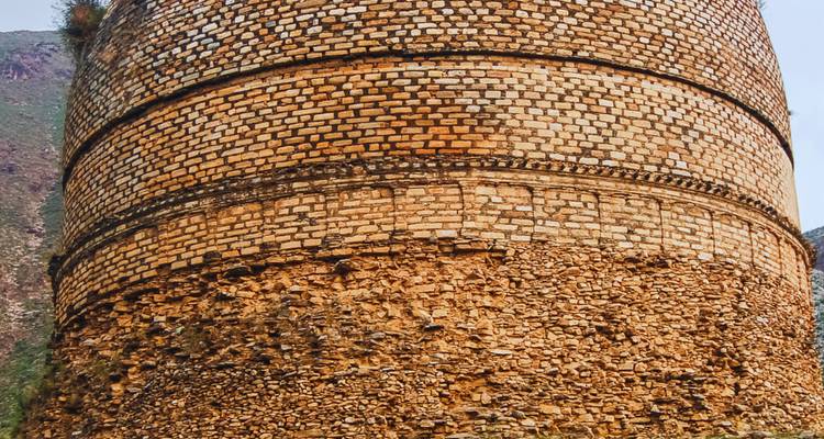 Un grand stupa circulaire en brique avec des assises superposées se dresse de manière proéminente contre le ciel.