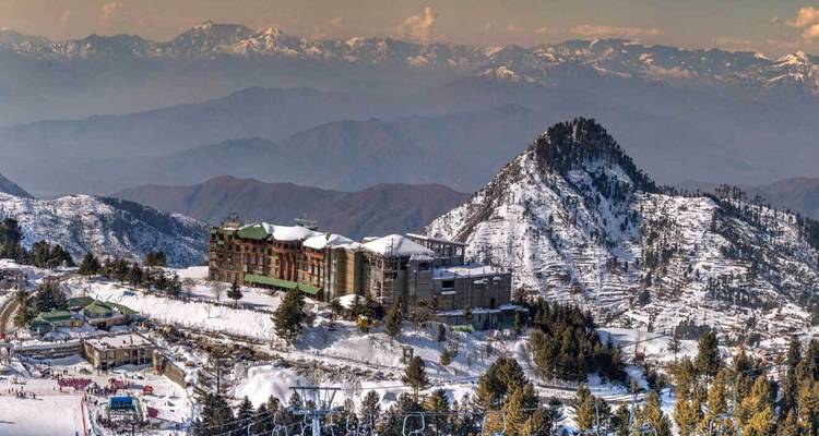Une station de montagne recouverte de neige se dresse sur une crête avec des pics spectaculaires s'étendant dans le lointain brumeux.