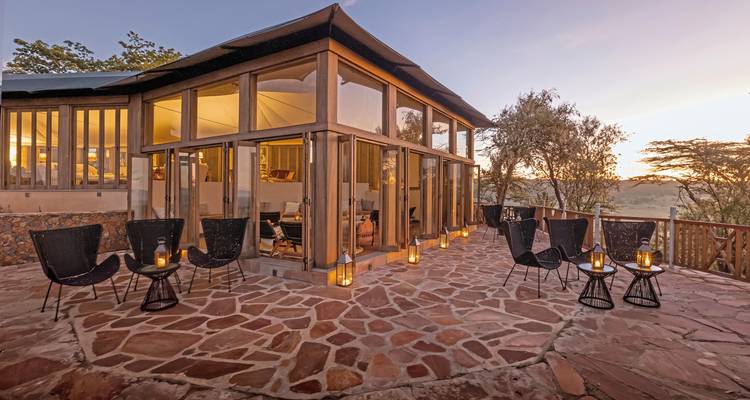 Außenbereich mit Sitzgelegenheiten, Glasgebäude und Laternen bei Sonnenuntergang.