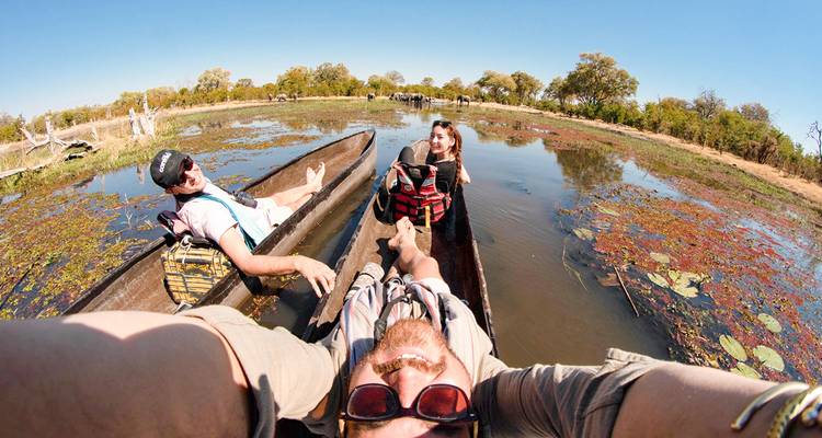 Personas relajándose en canoas sobre aguas poco profundas con vegetación alrededor.