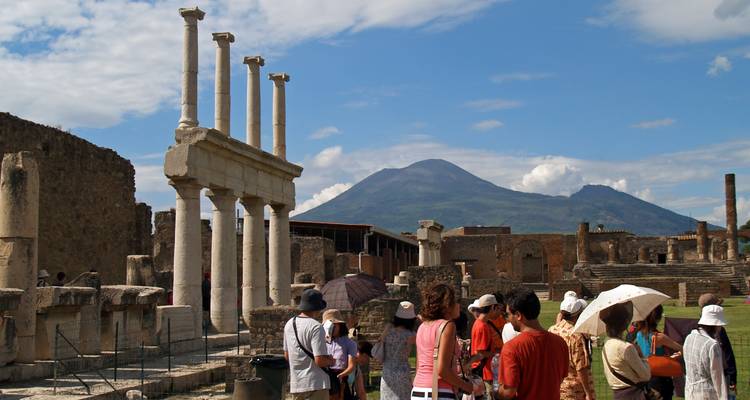 Groupe de personnes observant des ruines antiques avec une montagne en arrière-plan.