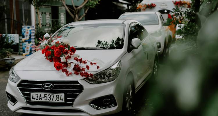 White car decorated with red flowers, likely for a wedding.