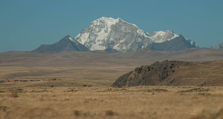 Paisaje montañoso con un gran pico nevado al fondo y llanuras onduladas en primer plano.