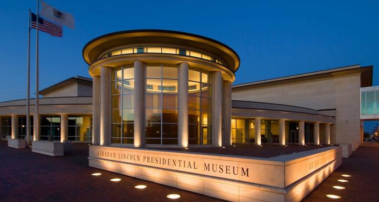 Fachada moderna e iluminada del Museo Presidencial Abraham Lincoln en Springfield al atardecer.