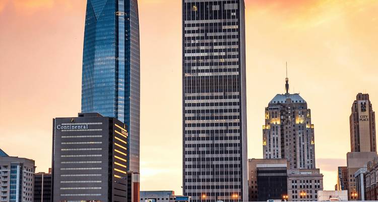 Horizonte de la Ciudad de Oklahoma con torres modernas y rascacielos iluminados por la luz cálida del atardecer contra un cielo lleno de colores.