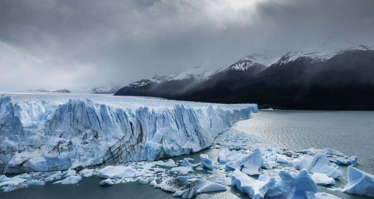 Vast glacier with dramatic clouds above a lake.