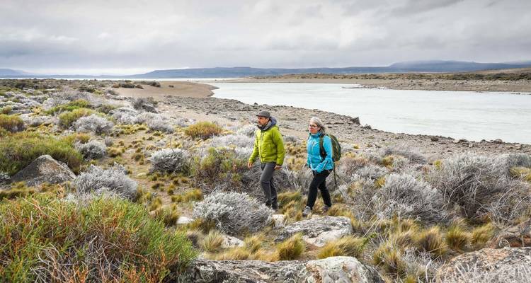 Two people hiking on rocky terrain by a river.