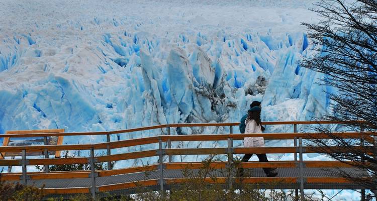 Person walking along a wooden path with a glacier backdrop.