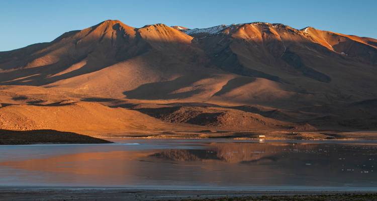 Des teintes dorées sur les montagnes se reflètent dans un lagon au coucher du soleil.