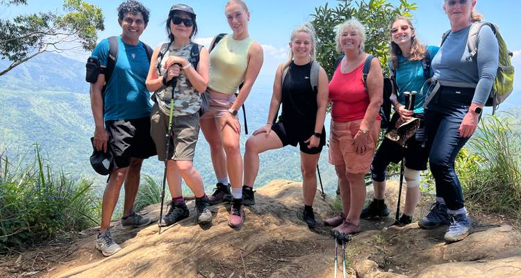 Glimlachende wandelgroep die poseert op een rotsachtige richel met mistige groene bergen achter hen.