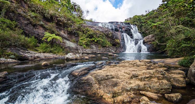 Waterval met meerdere niveaus stort zich in tropische stijl neer in een helder meer, omgeven door weelderig oerwoudgroen.