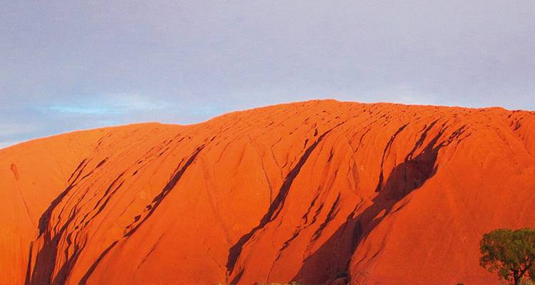 Primer plano de la masiva cara de arenisca roja de Uluru resplandeciendo bajo la suave luz del día con sutiles matices del cielo arriba.