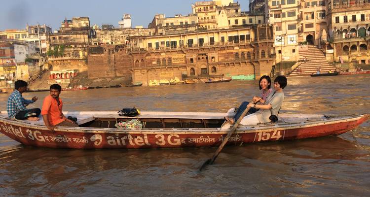 Bote de remos de madera con turistas se desliza por el río Ganges pasando los ghats históricos a la luz del atardecer.