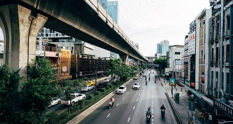 An urban cityscape with elevated transit tracks over a busy street.