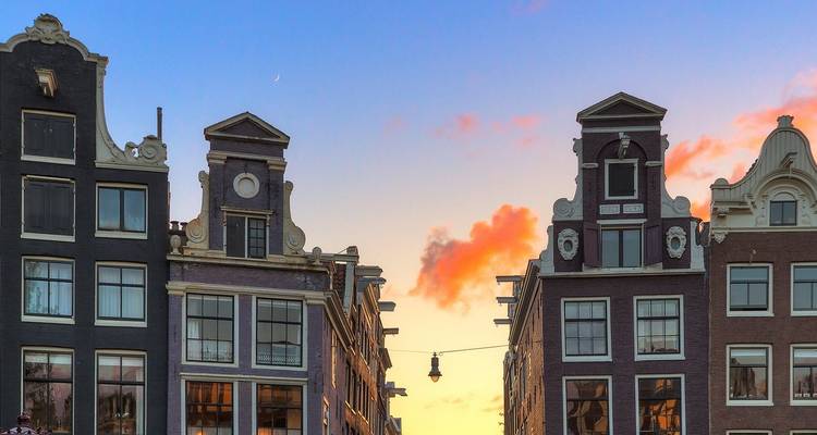 Cielo vespertino con luna creciente detrás de edificios de Ámsterdam con hastiales que brillan bajo la luz del atardecer