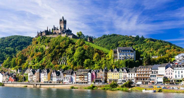 Vista brillante del Castillo de Cochem y el colorido pueblo ribereño reflejados en el Mosela bajo el cielo azul.