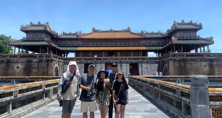 Famille debout sur un pont de pierre menant à l'imposante porte principale de la Citadelle impériale de Hué sous un ciel bleu dégagé.
