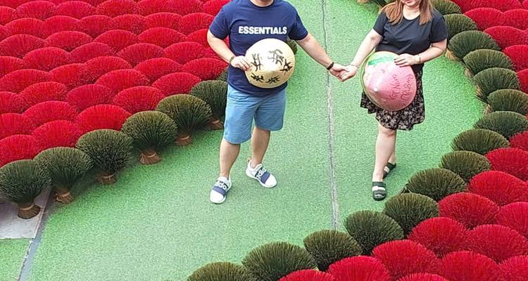 Jeune couple tenant des chapeaux coniques peints, debout parmi des fagots vibrants de bâtons d'encens rouges et verts disposés en rangées ordonnées.