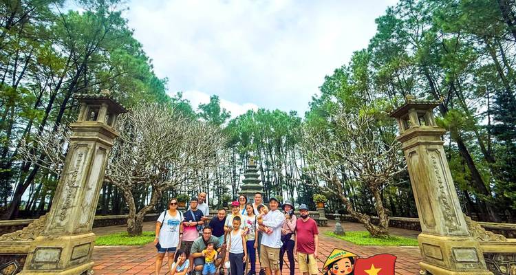 Groupe de touristes encadré par des piliers de pierre avec pagode en arrière-plan, scène identique avec filigrane de drapeau illustré.