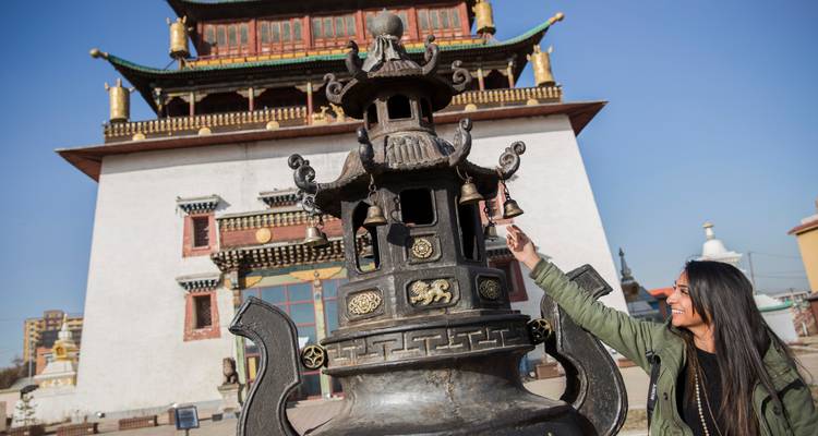Un viajero toca la campana de bronce de un quemador de incienso de un monasterio ornamentado bajo un cielo despejado.