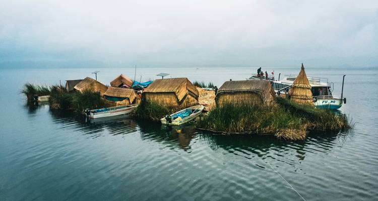 Groupe d'îles flottantes de roseaux avec de petits bateaux amarrés lors d'une matinée calme et brumeuse sur le lac Titicaca.