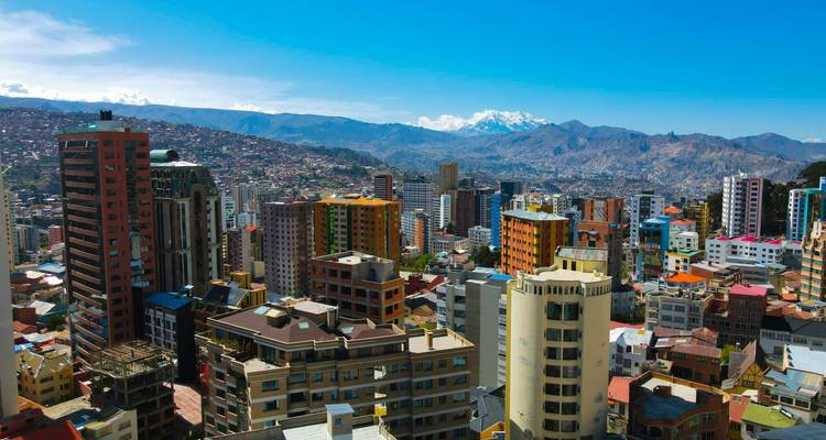 Skyline coloré de gratte-ciel de La Paz s'étendant à travers une vallée montagneuse sous un ciel bleu clair avec un pic enneigé au loin.