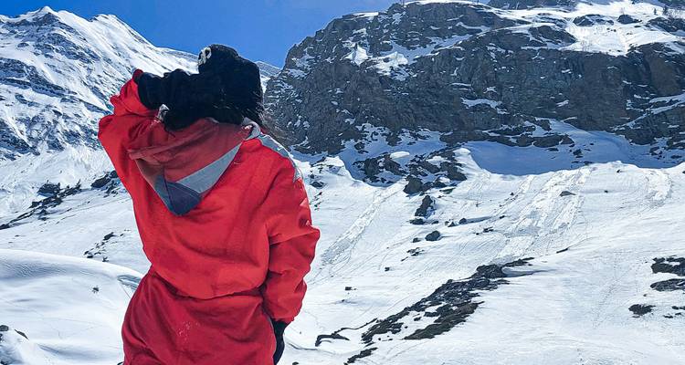Personne en manteau rouge regardant des montagnes enneigées.