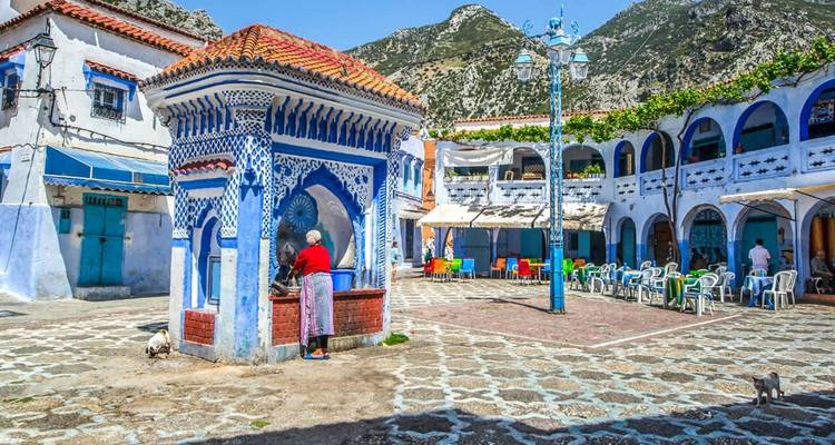 Bunter Innenhof mit einem Wasserbrunnen und Bergen im Hintergrund.
