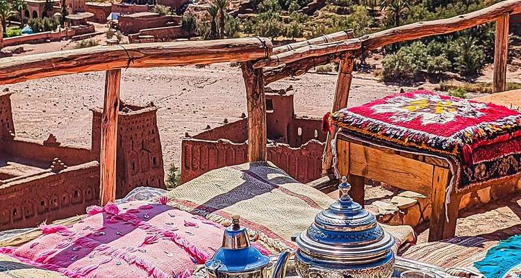 Marokkanisches Teeservice auf Kissen arrangiert mit Blick auf die Erdwälle von Ait Benhaddou.