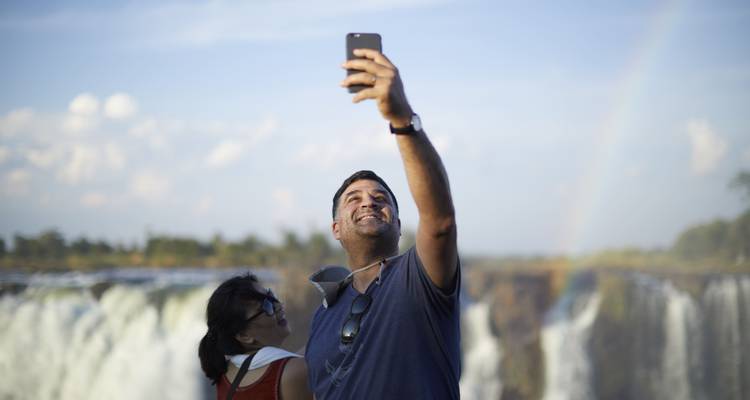 Deux personnes prenant un selfie avec un arc-en-ciel au-dessus des chutes d'Iguazú.