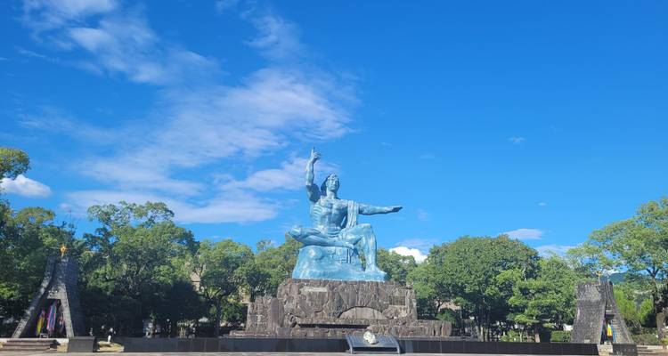 Het iconische Vredesstandbeeld rijst op tegen een levendige blauwe lucht in het gedenkpark van Nagasaki.
