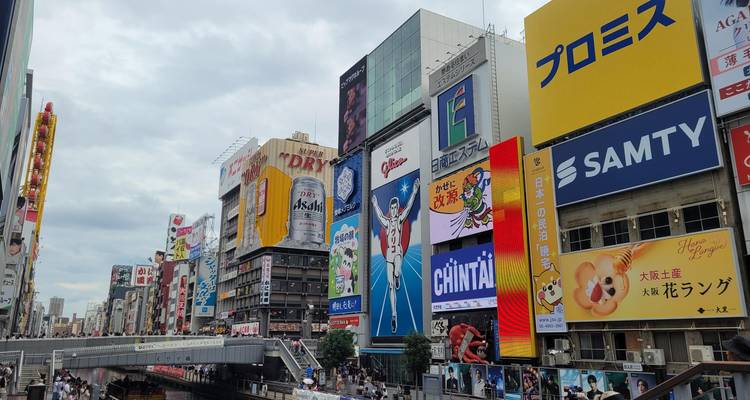 Neon billboards torenen boven Osaka's drukke Dotonbori kanaal uit onder bewolkte lucht.