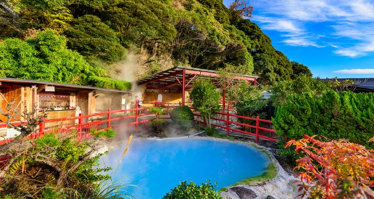 Piscine géothermale d'un bleu éclatant émettant de la vapeur à côté de garde-corps rouges et de jardins luxuriants.