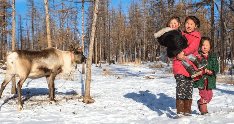 Eine Frau mit Kindern und einem Rentier in einem verschneiten Wald.