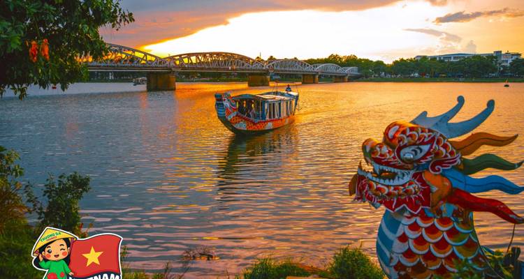 Un bateau décoré sur une rivière au coucher du soleil avec une vue sur un pont au loin.