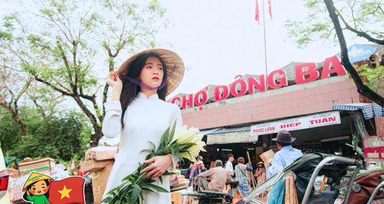 Une femme en tenue traditionnelle debout devant le marché Dong Ba.