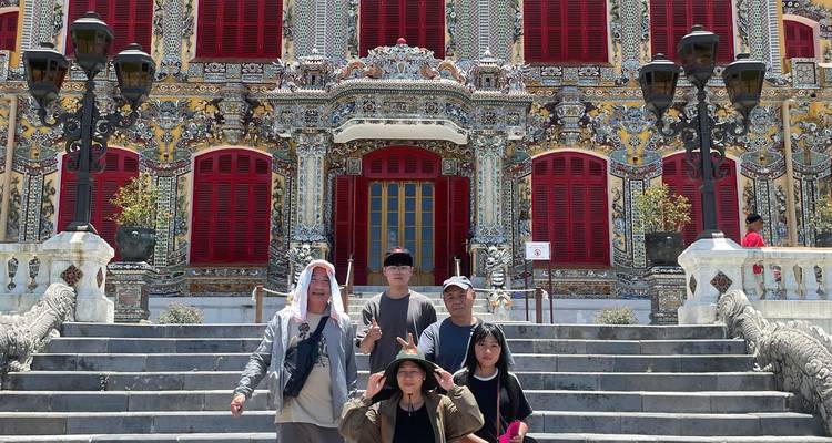Un grupo de viajeros posa frente a la fachada de un templo ornamentalmente decorado con contraventanas rojas vívidas en Hue.