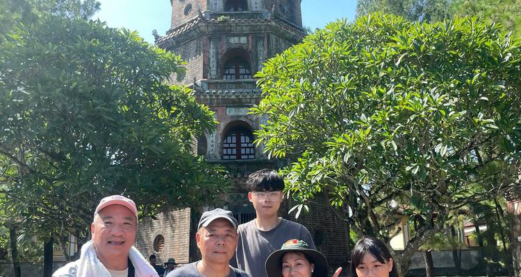 Grupo familiar posa bajo árboles frondosos con la torre de la Pagoda Thien Mu alzándose detrás.