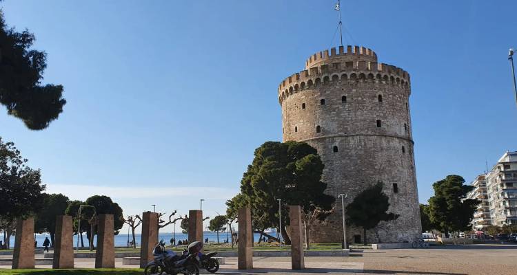 Der Weiße Turm von Thessaloniki mit Blick auf eine Promenade mit einem Motorrad und Fußgängern.