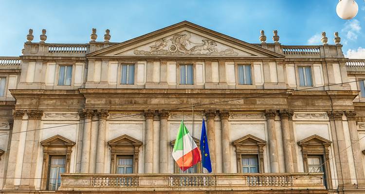 Neoklassieke gevel van het La Scala operagebouw met Italiaanse en EU-vlaggen onder een heldere hemel.
