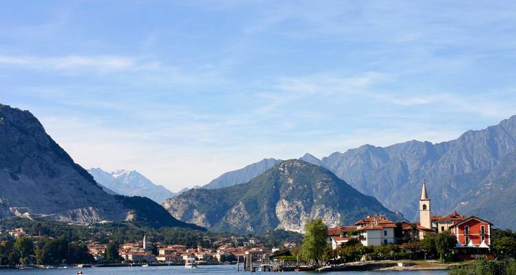 Petit village au bord du lac avec clocher d'église au pied des Alpes majestueuses et du ciel bleu.