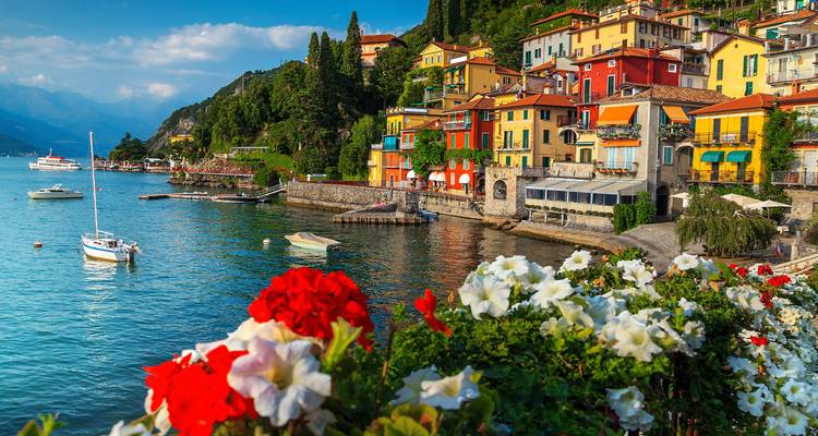 Les façades colorées du village du Lac Côme et les jardinières de fleurs se reflètent dans les eaux bleues et calmes lors d'un après-midi ensoleillé.