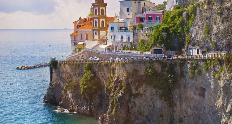 Pueblito de costa en lo alto del acantilado con una torre de iglesia en tonos pastel y casas en terraza que dan al resplandeciente Mar Tirreno en la Costa de Amalfi.