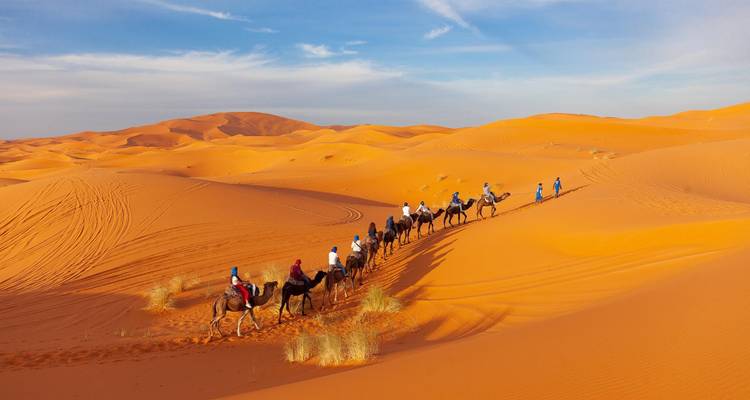 Des chameaux avec des cavaliers traversant une dune de sable.